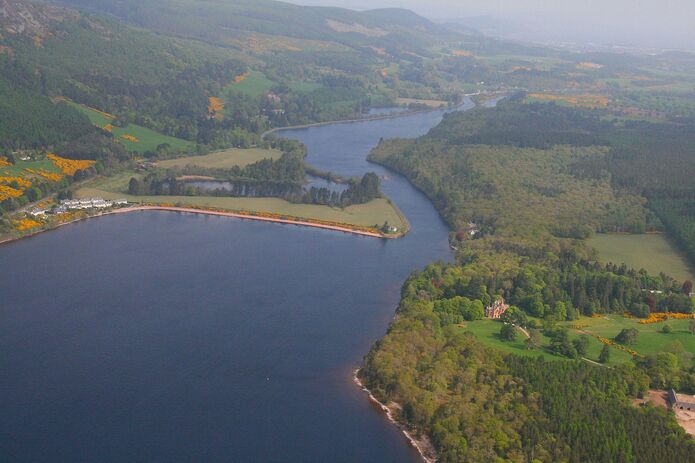 Aerial photo of canal with bend in the path next to forrest